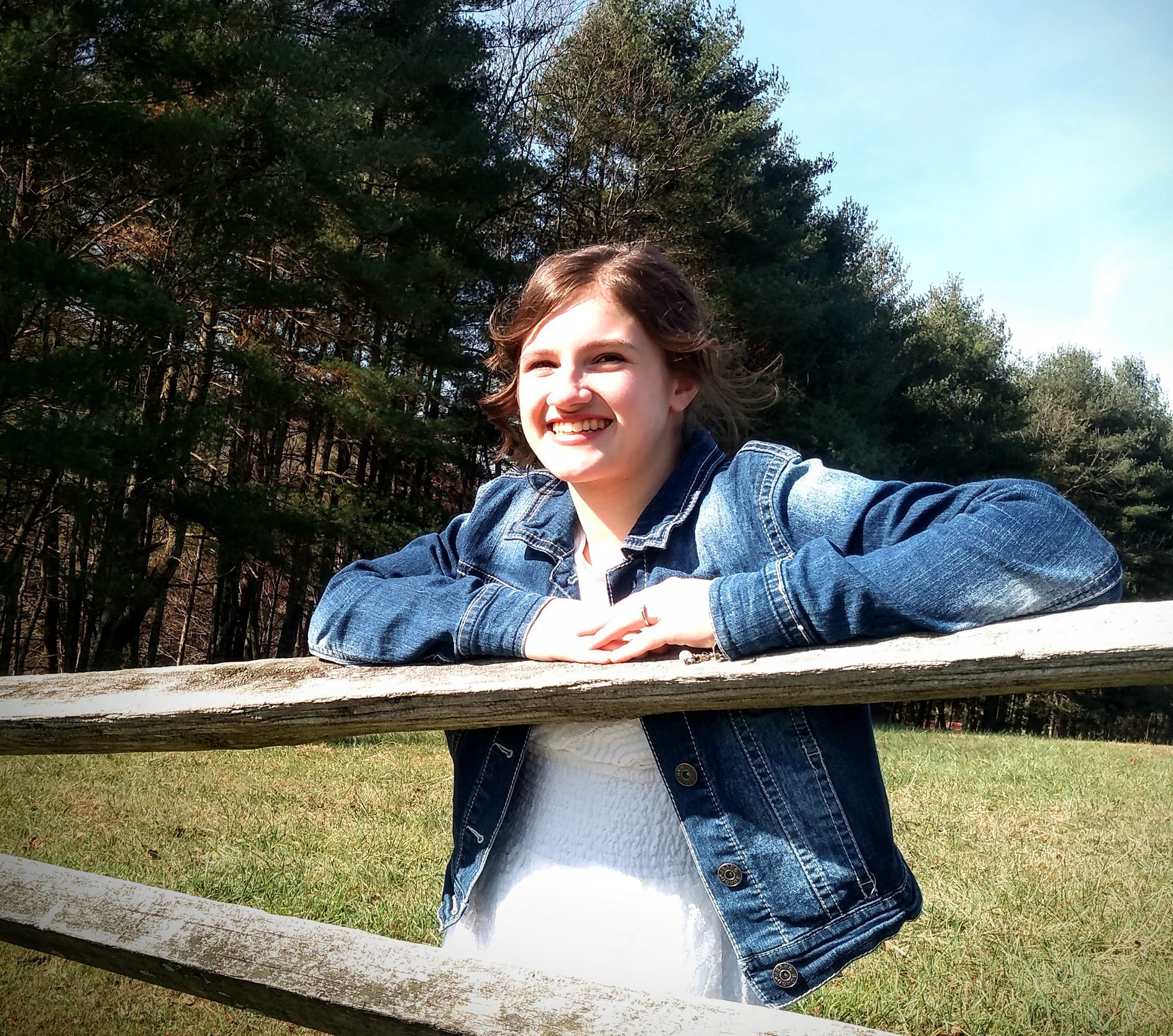Michala smiling with arms on a wooden fence in a field